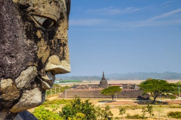 Buddha with a monastery in the background, Mrauk U, best Places to visit in Myanmar, southeast Asia